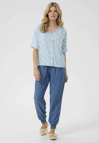 Modrá květinová košile s krátkým rukávem a knoflíky, doplněná volnými džínovými kalhotami na gumu. Outfit doplňují hnědé ploché boty.