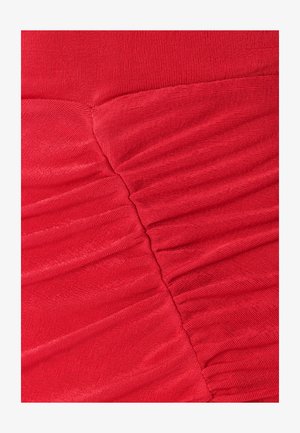 Nahaufnahme eines roten Stoffes mit strukturierten Falten und glatter Oberfläche, die kontrastierende Muster und ein zusammengeführtes Nahtdetail zeigt.