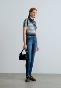 Tengerészkék és fehér csíkos galléros póló, hozzá illeszkedő kék farmernadrág. A modell egy kis fekete kézitáskát tart, és leopárdmintás tornacipőt visel.