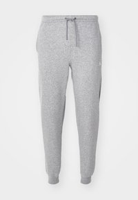 Světle šedé tepláky s elastickými manžetami, šňůrkovým pasem, bočními kapsami a malým bílým logem Jumpman na levém stehně.