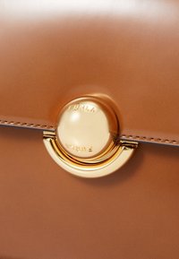 Ruskean nahkalaukku, jossa on sileä pinta, kultainen pyöreä solki, jossa on kaiverrus "FURLA", sekä sopivat varusteet.