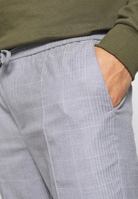 Světlé šedé kalhoty s vzorem rybí kosti a jemným kostkovaným designem, s elastickým pasem a boční kapsou.