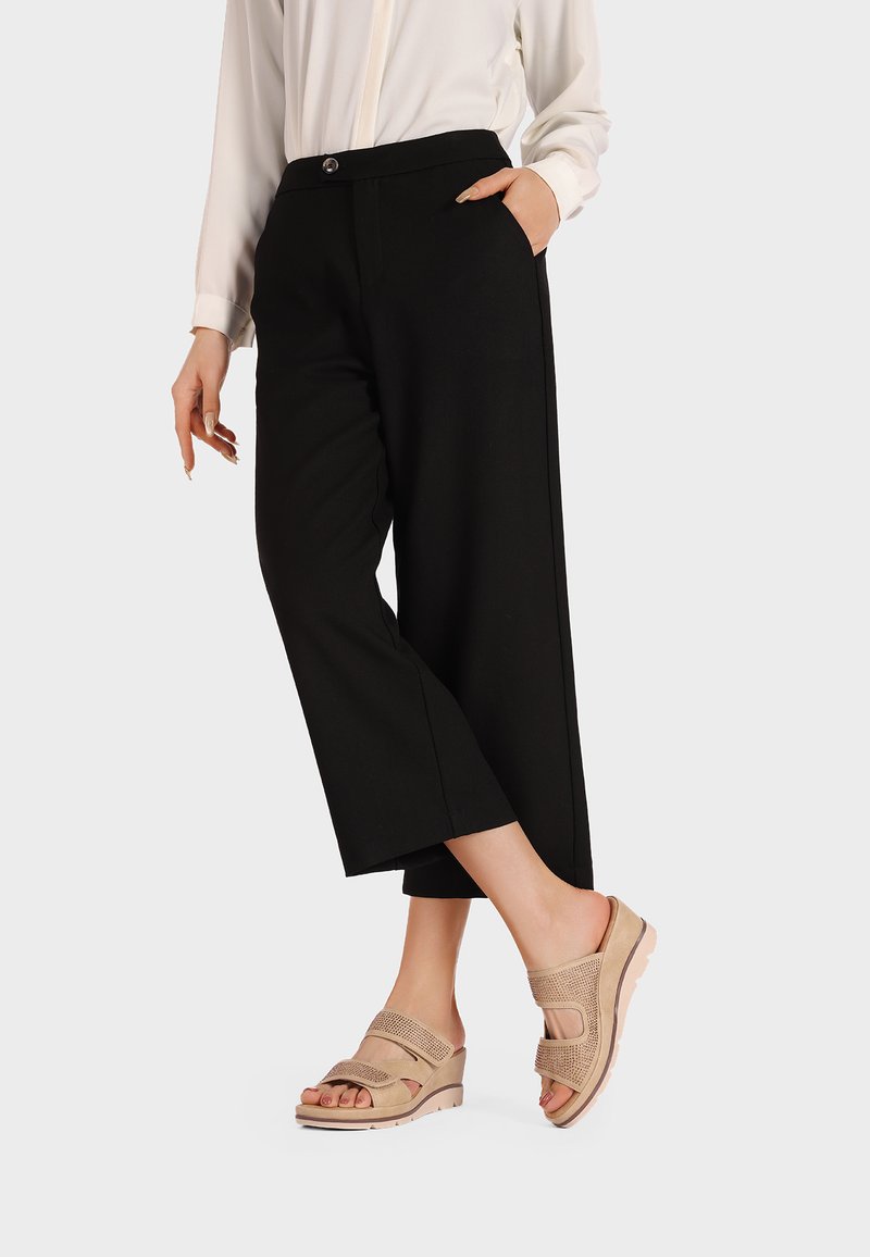 Pantaloni neri a gamba larga realizzati in un tessuto morbido, dotati di tasche laterali e chiusura con bottone, abbinati a sandali con zeppa beige arricchiti da dettagli in rete.