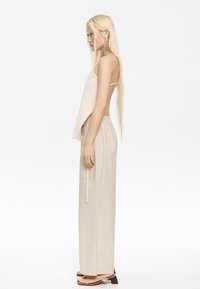 Beige ribbed tank top with thin straps, paired with light beige wide-leg pants featuring an elastic waistband and side pockets, worn with flat sandals.