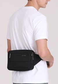 Borsetta nera in vita con superficie testurizzata, dotata di due tasche con zip e cinturino regolabile. Logo del marchio visibile sulla parte anteriore.