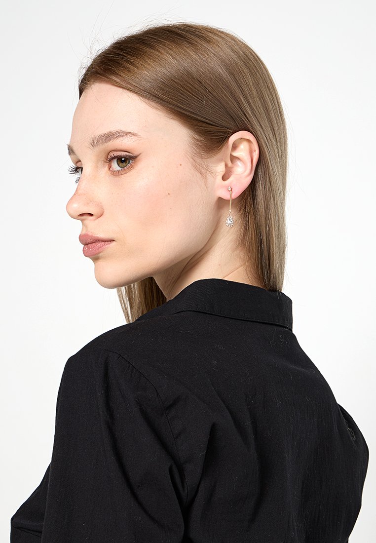 Orecchini a pendente in tono oro con un pendente di gemma trasparente, caratterizzati da un design elegante e un elemento a catena delicato.