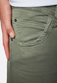 Pantalones de mezcla de algodón verde con una textura suave. Cuentan con un bolsillo frontal con detalles de costura y un acento decorativo metálico.