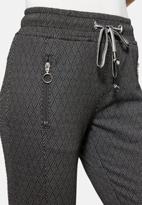 Graue Jogginghose mit einem diamantartigen Muster, verstellbarem Kordelzug und zwei Reißverschlusstaschen an den Seiten, die mit metallischen Hardware-Elementen versehen sind.