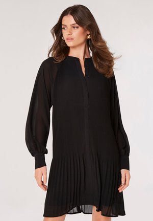 Black pleated dress with a buttoned front, long balloon sleeves, and a textured fabric. Hemline curves slightly at the bottom.