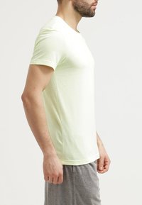 Camiseta de manga corta de color amarillo claro con un patrón texturizado en los hombros, cuello redondo y un corte relajado. Combinada con pantalones cortos grises.