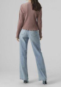 Záhybový mauve top s dlouhými rukávy, kombinovaný s džíny z lehkého modrého denimu s vysokým pasem. Textura je hladká a design je ležérní.