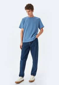 Blå bomulds T-shirt med rund halsudskæring, parret med mørkeblå denimjeans og cremefarvede sneakers med gummisål. 
