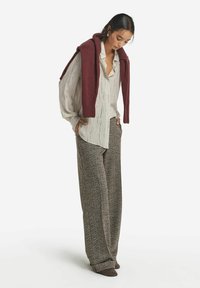 Långa, löst sittande mönstrade byxor i jordnära färger, parat med en ljus, texturerad vit skjorta och en vinröd tröja hängande över axlarna.