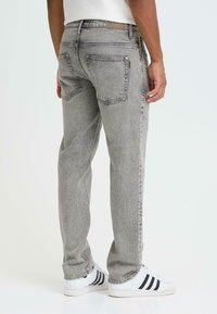 Jean en denim gris à coupe droite, avec deux poches arrière, une boucle pour ceinture et une texture subtilement délavée. Porté avec des baskets blanches.