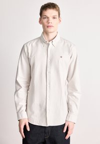 Ανοιχτό μπεζ πουκάμισο με κάθετες ρίγες, βαμβακερό ύφασμα, μακριά μανίκια, γιακάς με κουμπιά και μικρό κεντημέ�νο λογότυπο στο στήθος.