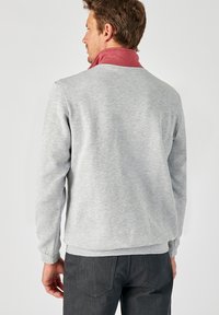 Sudadera gris con un cuello rojo, mangas largas y puños acanalados. La parte posterior presenta una textura suave, sin patrones ni adornos.
