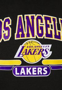 T-shirt nera con la scritta "LOS ANGELES LAKERS" in grassetto, in caratteri viola e gialli, e un grafico di un pallone da basket al centro.