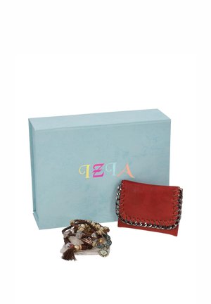 Una cartera de piel roja con adornos de cadena y un montón de pulseras de cuentas están delante de una gran caja de regalo azul claro.