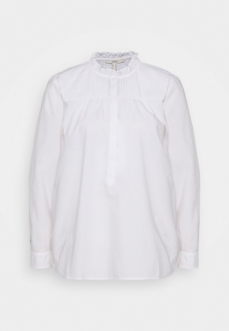 Blouse blanche à manches longues avec un col montant à volants, des plis verticaux sur le haut de la poitrine et une patte de boutonnage cachée à l’avant.