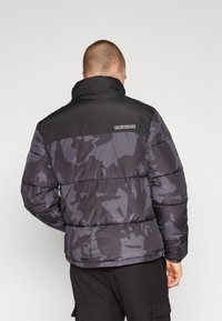 Giubbotto imbottito in camouflage grigio e nero, con colletto alto e design trapuntato. Logo del marchio ricamato sul retro.