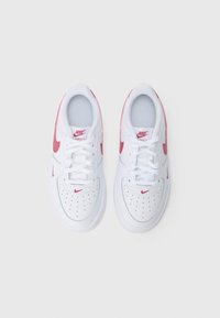 Balts Nike Air Force 1 kedas ar sarkaniem swoosh logo, sasieti šņores, skatīti no augšas uz vienkārša balta fona.