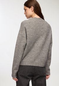 Szary, dziany sweter z szerokim okrągłym dekoltem, ściągaczami na mankietach i u dołu. Tekstura jest miękka, a fason wydaje się luźny.