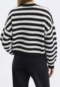Maglione in maglia a righe bianche e nere con silhouette corta e orlo a costine. Presenta un motivo texturizzato e maniche a vestibilità ampia.