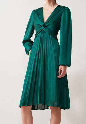 Zielona plisowana sukienka midi z długimi bufkami i ozdobnym skrętem w talii przy głębokim dekolcie w kształcie litery V.