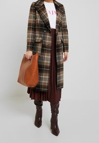 Rutig ullkappa i bruna, svarta och krämfärgade nyanser; tillsammans med en vinröd plisserad kjol. Brun läderväska och bruna knähöga stövlar.