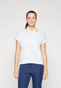 Polo a maniche corte bianco con colletto caratterizzato da un bordo beige e tre bottoni, abbinato a pantaloni blu navy. Design semplice e lineare.