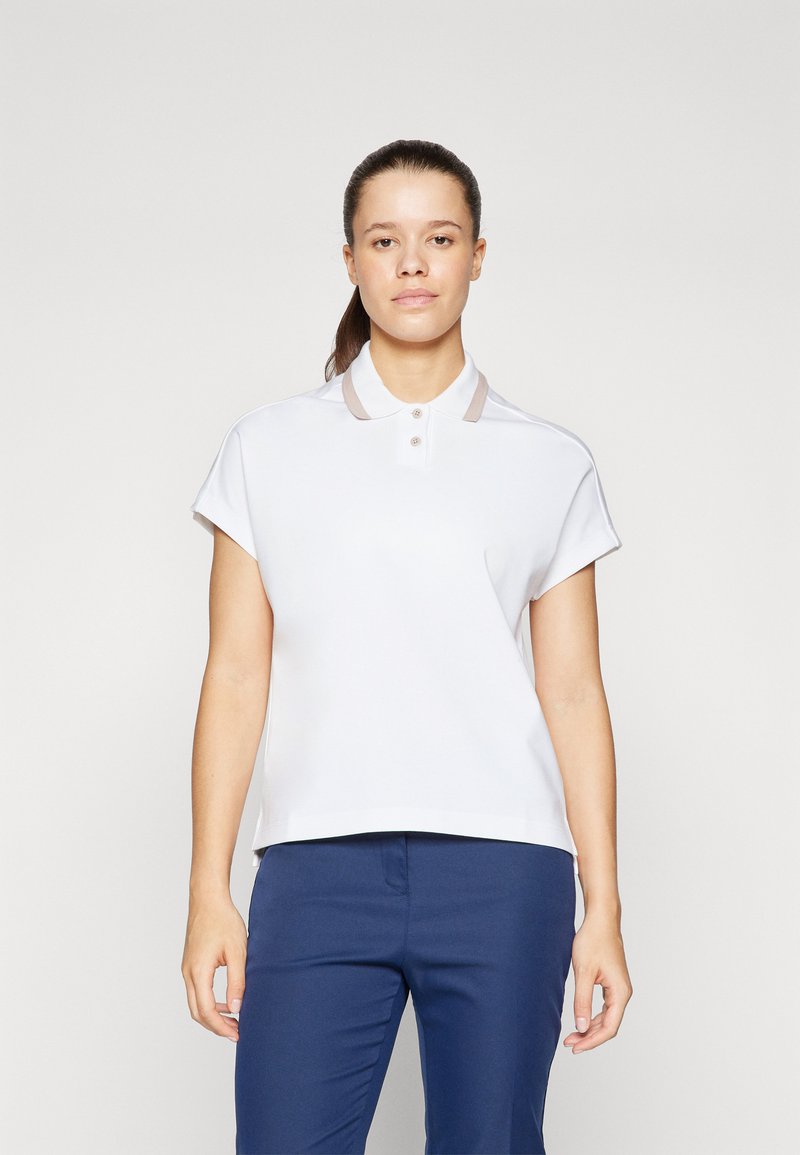 Polo a maniche corte bianco con colletto caratterizzato da un bordo beige e tre bottoni, abbinato a pantaloni blu navy. Design semplice e lineare.
