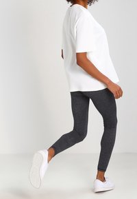 Vit kortärmad topp med lös passform, i kombination med slim fit mörkgrå leggings och vita sneakers, som visar en avslappnad och bekväm outfit.