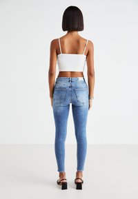 Μπλε στενά τζιν από τζην με ξεθωριασμένο φινίρισμα, μέση σε μεσαίο ύψος και δύο πίσω τσέπες, συνδυασμένα με ένα λευκό κοντό τοπ.