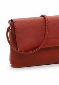 Red leather crossbody bag with a flap closure, zippered top, and a round handle. Features a smooth texture and subtle logo detail.