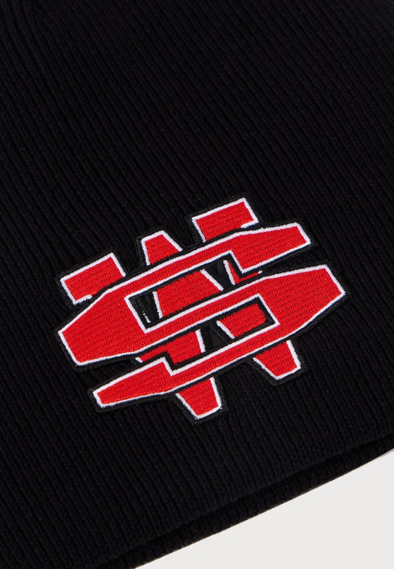 Bonnet en tricot noir à côtes avec un grand logo brodé rouge et blanc, présentant des formes géométriques, créant un contraste audacieux et un design texturé.