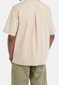 Beige overhemd met korte mouwen met een rugplooidesign, gemaakt van textuurstof. Heeft een rechte zoom en een relaxte pasvorm.