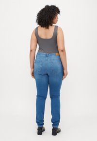 Pilkas bodysuit'as suderintas su mėlynomis siaurėjančiomis kelnėmis. Kelnės turi vidutinį juosmens aukštį, galinius kišenes ir šviesiai rudos odos etiketę ant juosmens. Juodi bateliai.