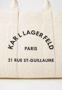 Plátěná taška v krémové barvě s černým textem. Zobrazuje "KARL LAGERFELD", "PAŘÍŽ" a "21 RUE ST-GUILLAUME" v tučném moderním písmu.