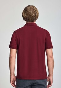 Mörkröd polo skjorta med ett texturerat mönster, korta ärmar och ribbad krage. Utsikten visar baksidan och avslöjar en avslappnad, skräddarsydd passform.