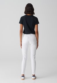 Camiseta negra de manga corta, jeans ajustados blancos y zapatillas blancas con detalles en azul marino. La vista trasera muestra la forma ajustada y la textura suave de la tela.