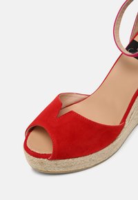 Sandale compensée en daim rouge avec bout ouvert, bride de cheville bordée de rose et semelle plateforme en jute tressé.