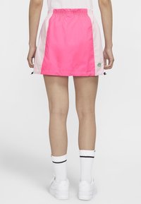 Rosa och ljusrosa nylon idrottskjol med elastisk midja, med sidofickor och en liten logodetalj nära fållen.