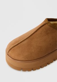 Barna, slip-on cipő sima bőr felsőrésszel, lekerekített orral és vastag, struktúrált talppal. Jellemzője a látható varrás az illesztés mentén.