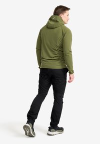 Green hooded sweatshirt with a smooth texture, paired with black pants featuring cargo pockets and elastic cuffs. Footwear has a rugged sole.