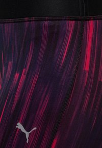 Legginsy Puma z czarną tasiemką w talii oraz dynamicznym, abstrakcyjnym wzorem w kolorze fioletowym i czerwonym, wykonane z elastycznej, gładkiej tkaniny.