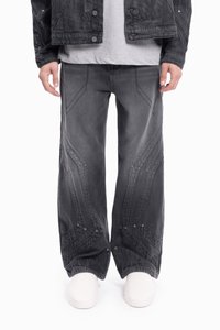 Czarna kurtka dżinsowa o teksturowanym wykończeniu, w połączeniu z szarymi spodniami o szerokich nogawkach, z kontrastowymi przeszyciami i geometrycznymi wzorami.