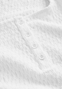 Gros plan d'un tissu blanc texturé avec quatre boutons blancs alignés verticalement au centre.