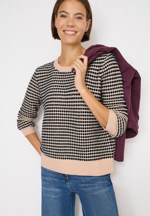 Maglione lavorato a maglia con un motivo a cuori rosa e navy, polsini e orlo a costine, indossato con jeans di denim, completato da una giacca viola portata sulle spalle.