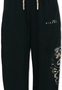 Pantalon de survêtement noir avec une taille à cordon orné d'accents métalliques. La jambe gauche présente un motif détaillé orné de dessins floraux et de serpents.