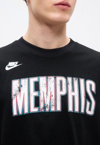 Μαύρο βαμβακερό μπλουζάκι με μεγάλο, φθαρμένο κείμενο "MEMPHIS" σε λευκό, κόκκινο και μπλε, με μικρό λευκό λογότυπο Nike στον ώμο.